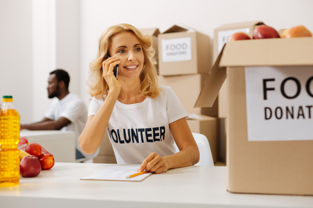 Woman using her phone with boxes of donated food in the foreground and background