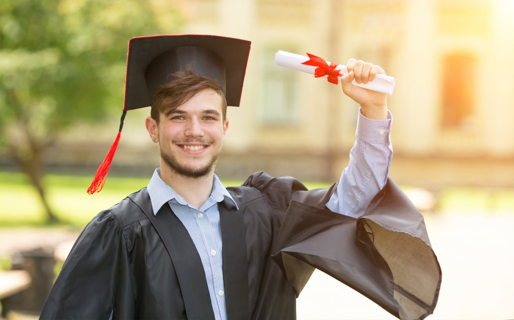 Student wearing graduation regalia with a rolled up diploma in his hand while he is on campus