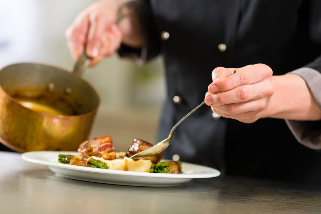 Chef preparing to pour gravy into a dish of meat and vegetables.