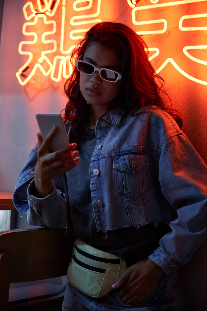 A woman in 80s-inspired fashion wearing sunglasses, a cropped but oversized denim jacket, denim pants, and a fanny pack