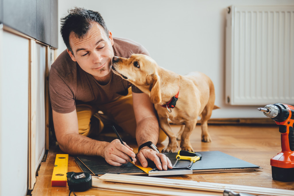 A man getting licked by his dog while measuring panels for a renovation