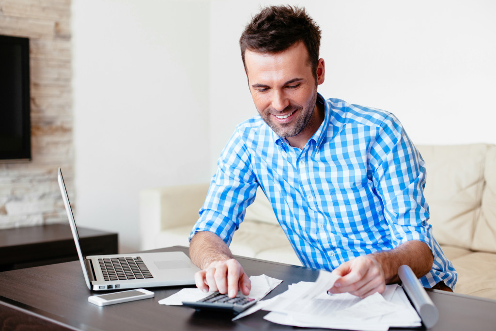 male professional using calculator and laptop to analyze his expensses