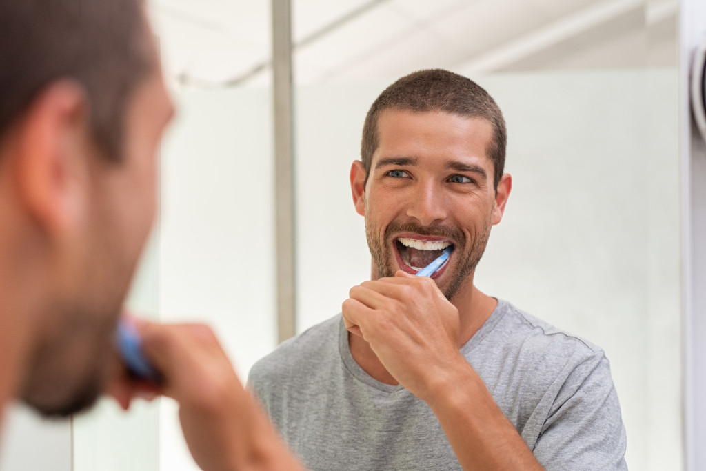 man cleaning teeth and looking at mirror