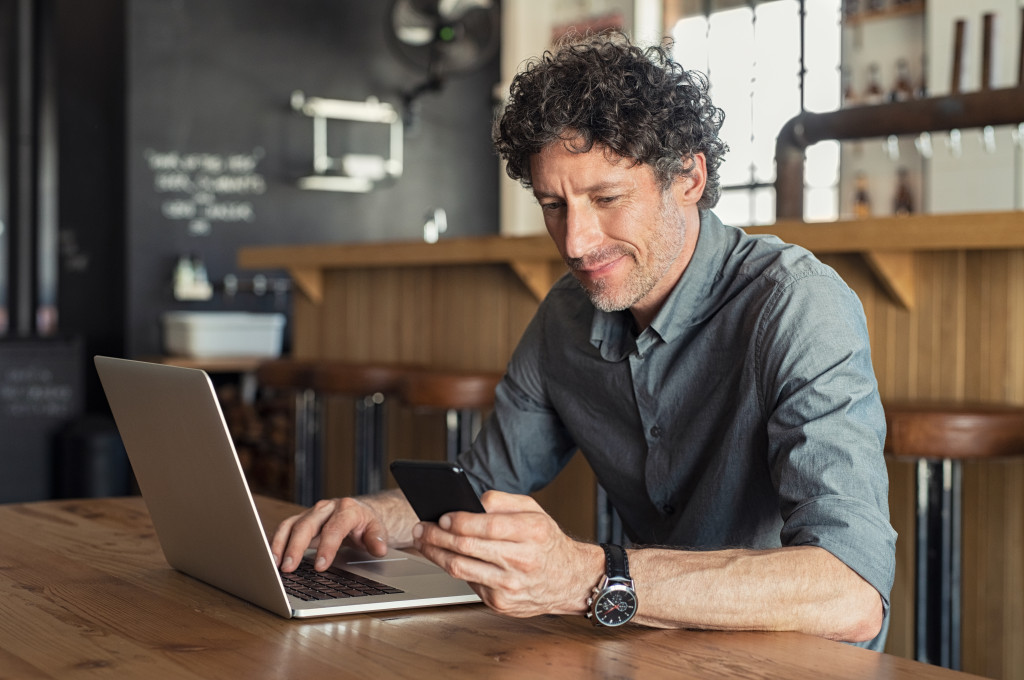 An owner or manager busy with work using a phone while using a laptop