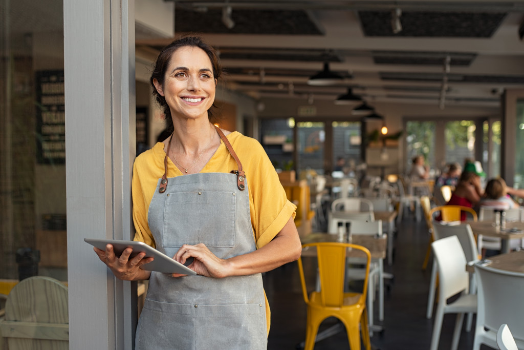 business woman standing in the entrance of restaurant while holding a tablet