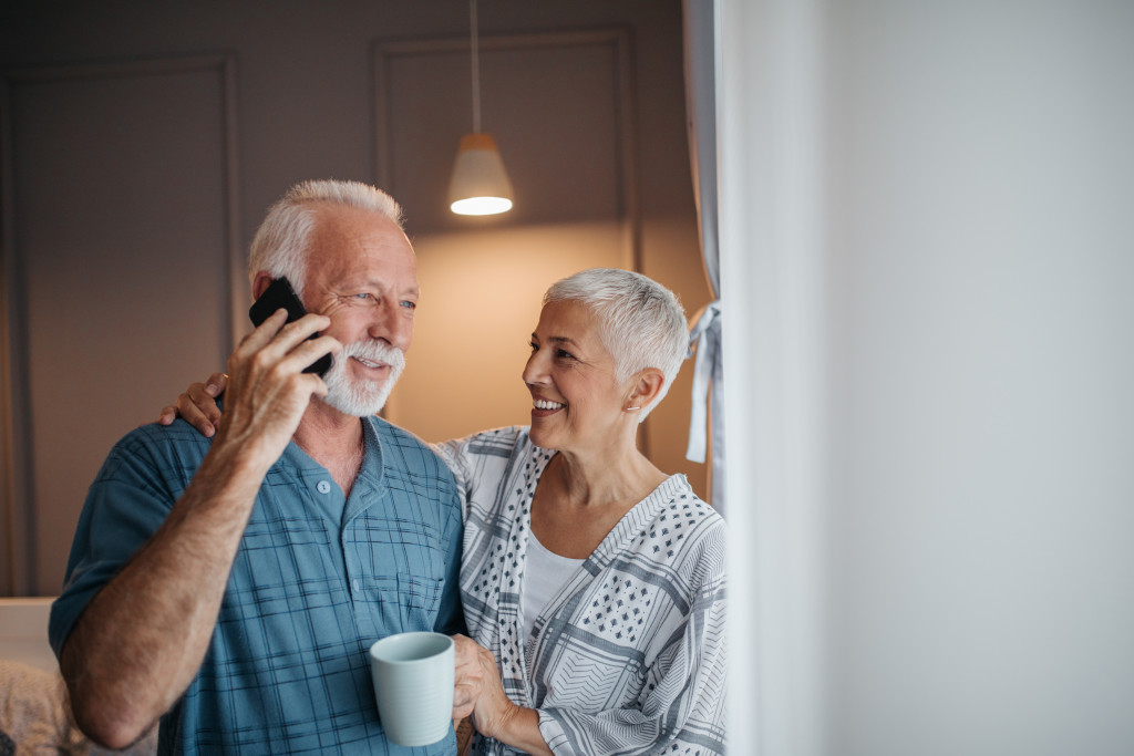 senior couple laughing while man talks to someone using smartphone in kitchen