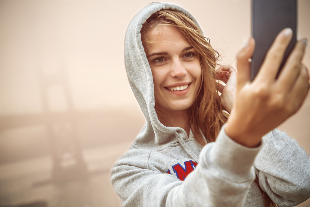 Young woman smiling while taking a selfie with a fog-covered bridge in the background.