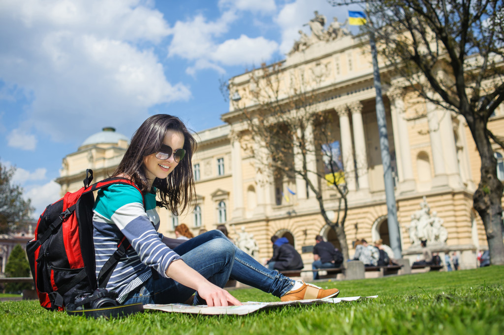 Young woman checking a map while sitting on grass at a park.