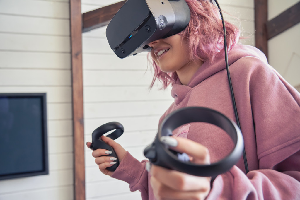 Young woman wearing a VR headset goggles while holding game controllers.